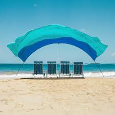 Beach scene with four chairs under a blue canopy facing the ocean.